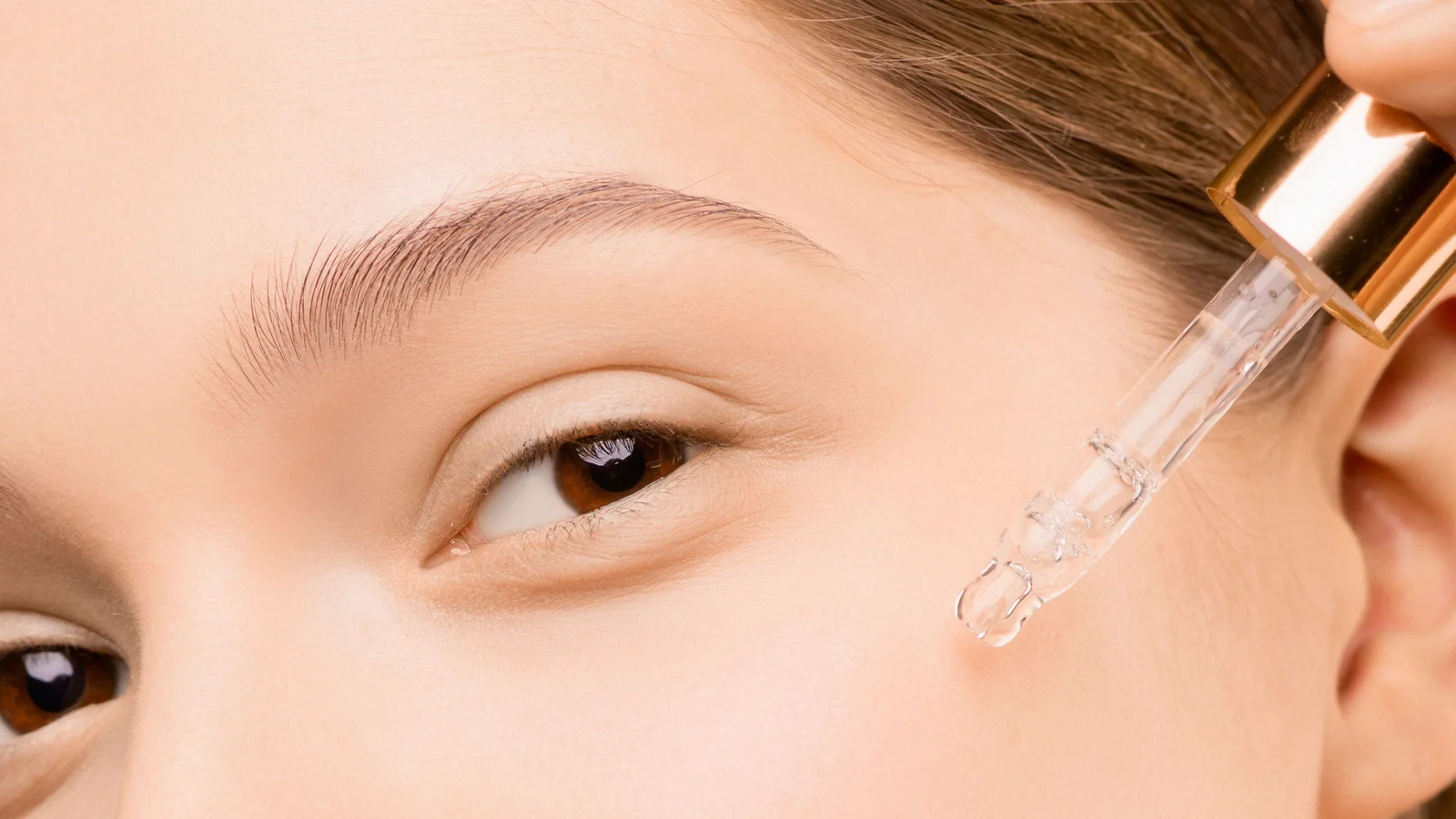 Castor oil serum being applied to facial skin with a glass dropper
