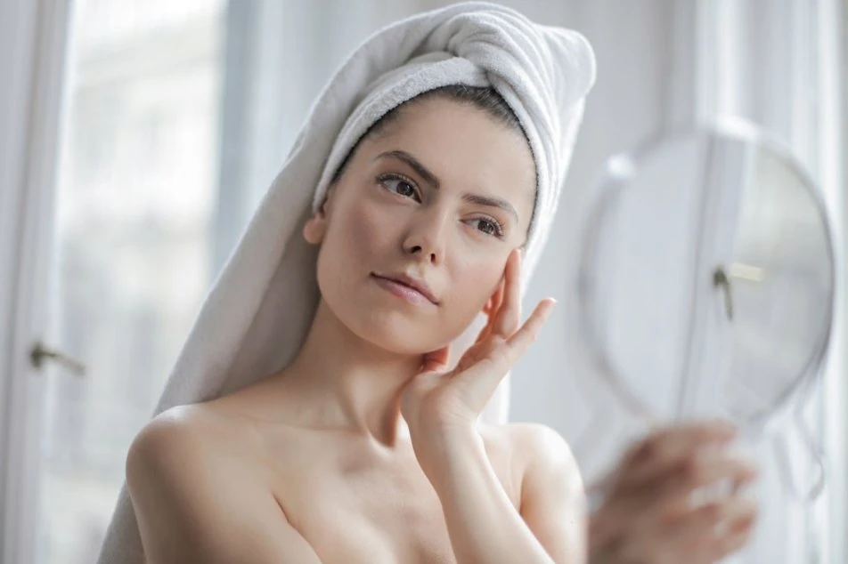 Woman with healthy hydrated skin examining her face in a hand mirror