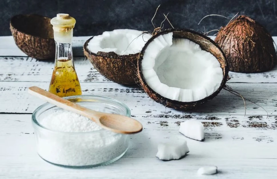 Refined or unrefined coconut oil for skin in a glass bottle beside fresh coconut