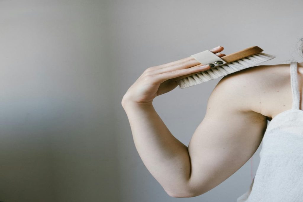Woman dry brushing her upper arm to treat small bumps on the arms and keratosis pilaris